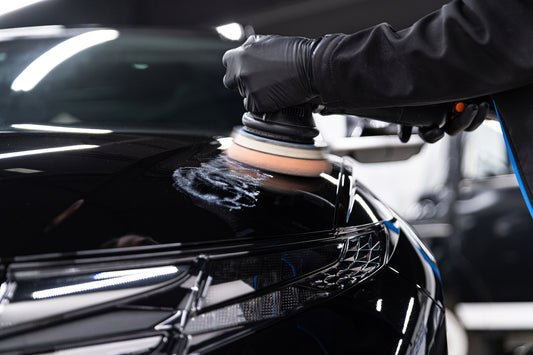 Professional auto detailer using a high-speed buffer to apply wax on a car's surface for a glossy and protective finish.